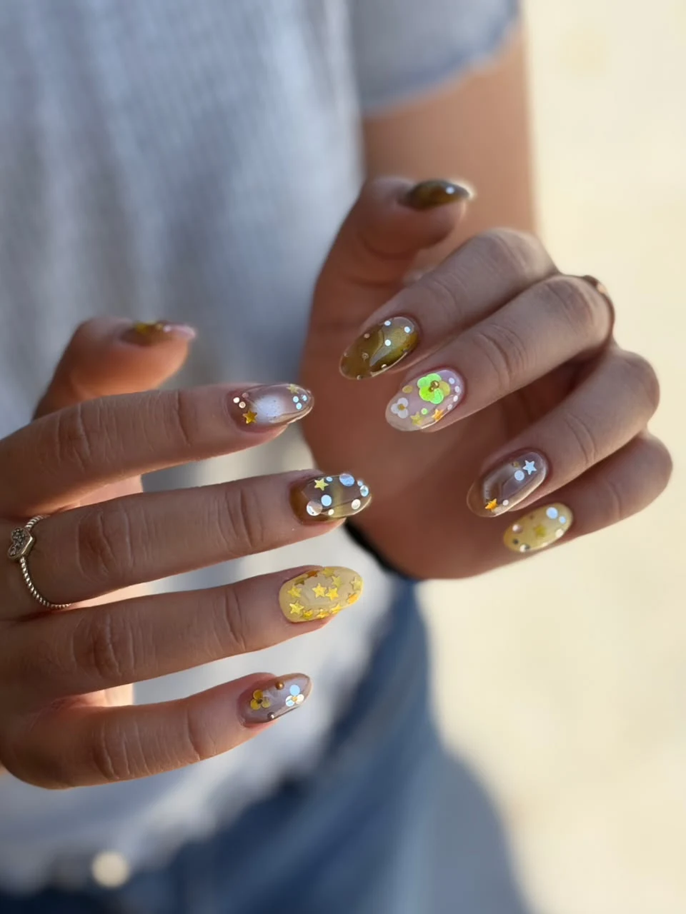 Manicura en tonos tierra, dorado y detalles luminosos.